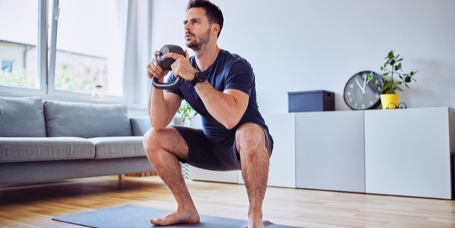man doing squats with kettlebell weights at home.